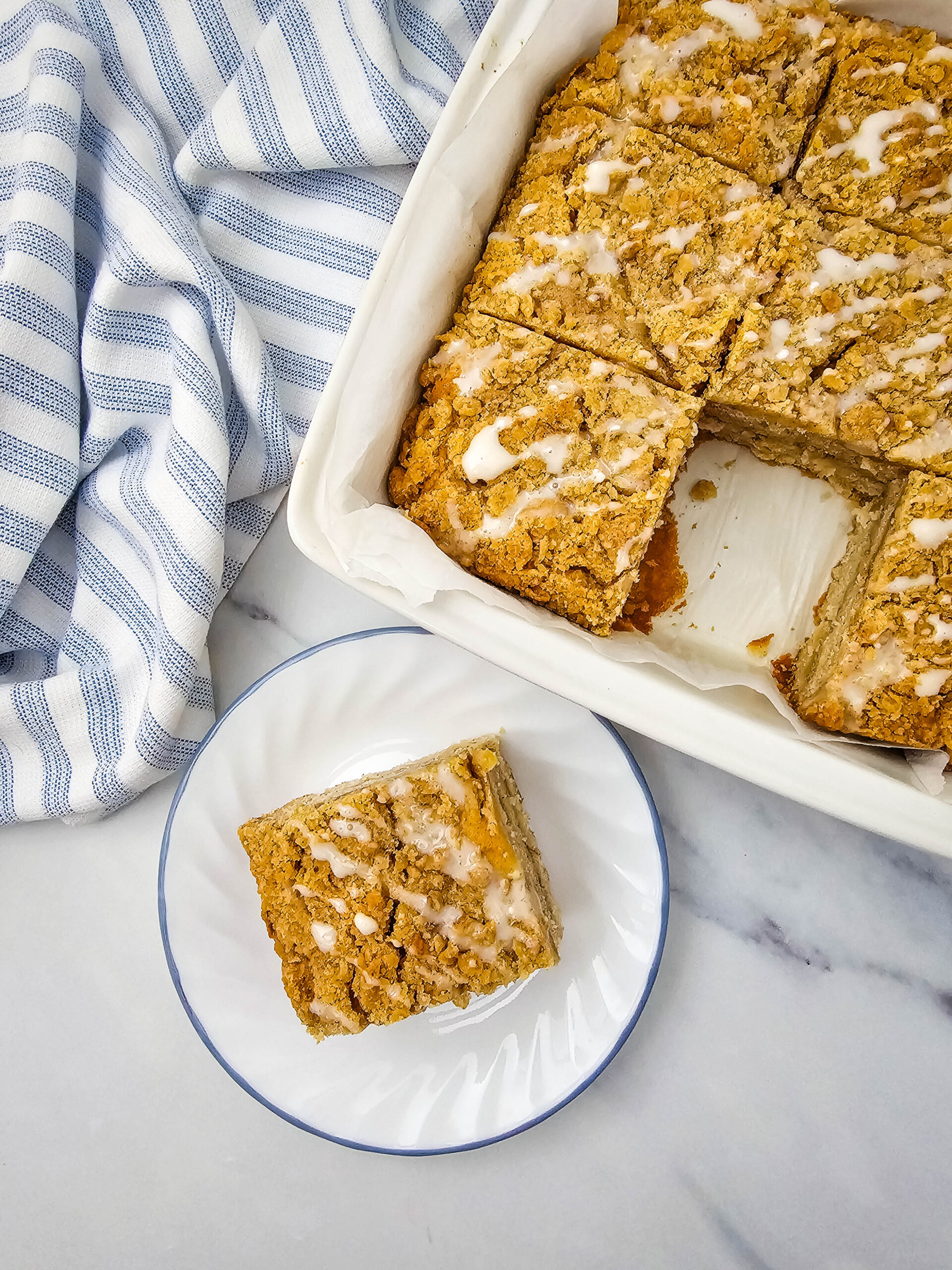apple crumb cake in a pan with one slice cut out and placed on a white plate.
