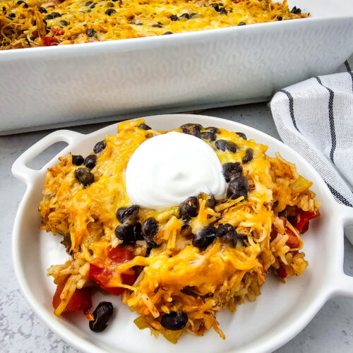 chicken taco casserole on a white plate with a dollop of sour cream on top.