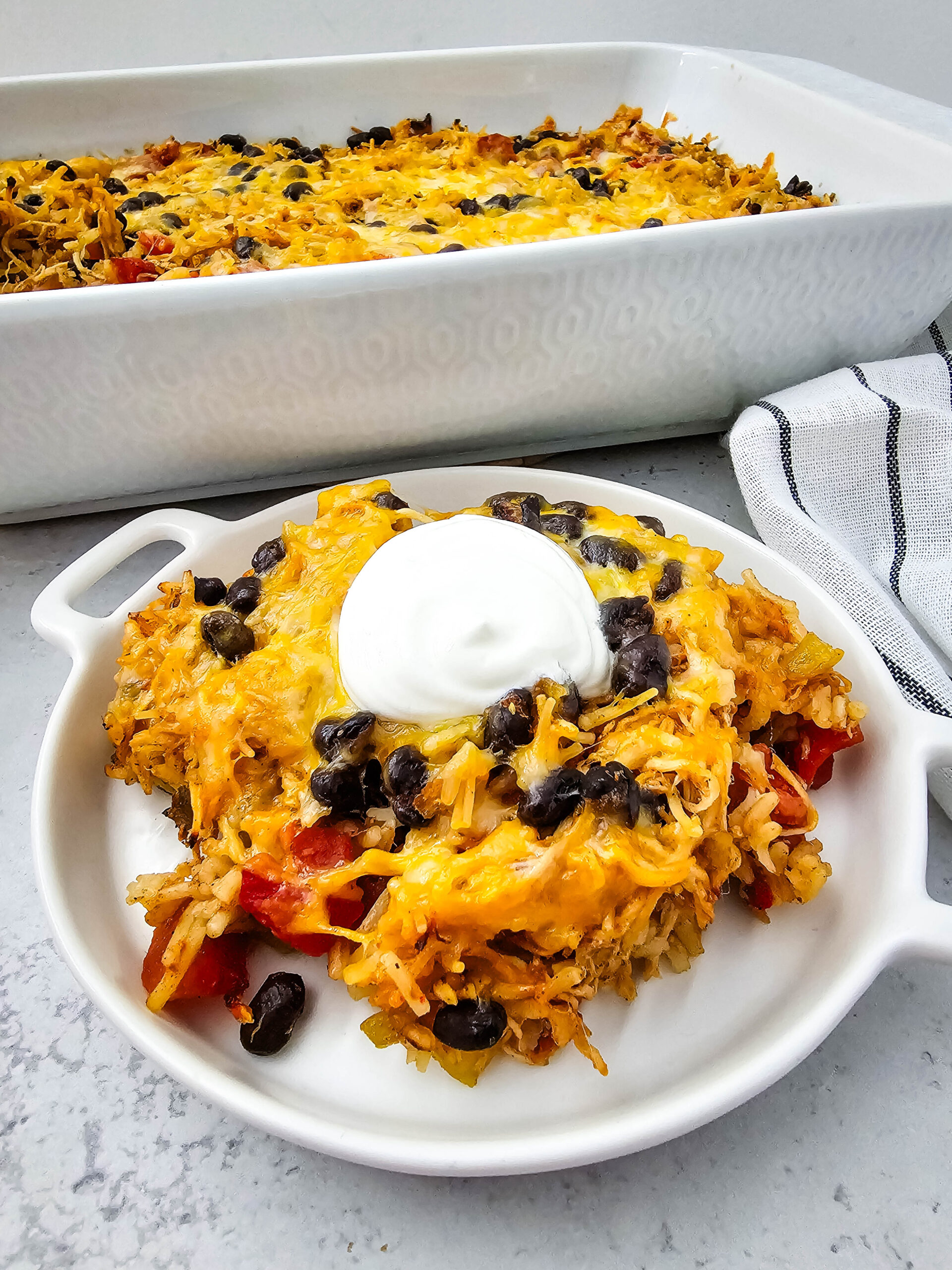 chicken taco casserole on a white plate with a dollop of sour cream on top.