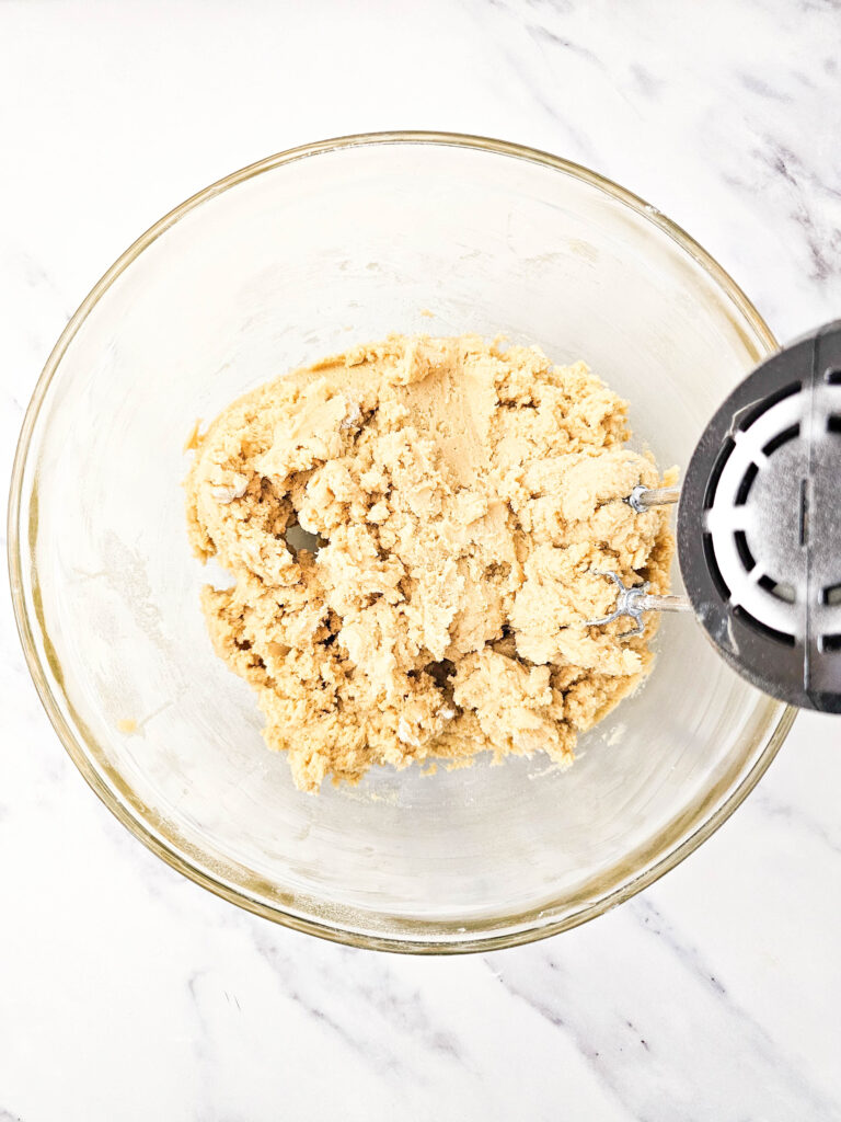 beaten cookie dough in a glass bowl with a hand mixer.