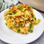 Close-up of creamy Chicken Noodle Casserole with egg noodles, shredded chicken, peas, green onions, and buttery cracker crumbs.