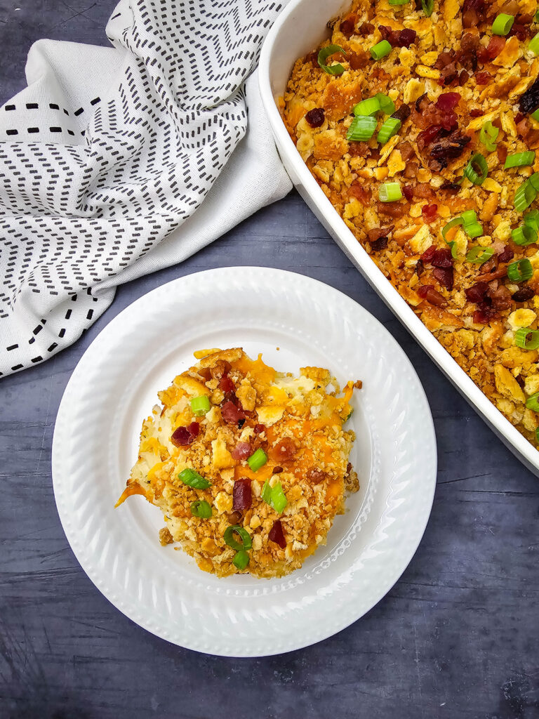 Serving of Million Dollar Potato Casserole on a white plate beside the casserole dish.