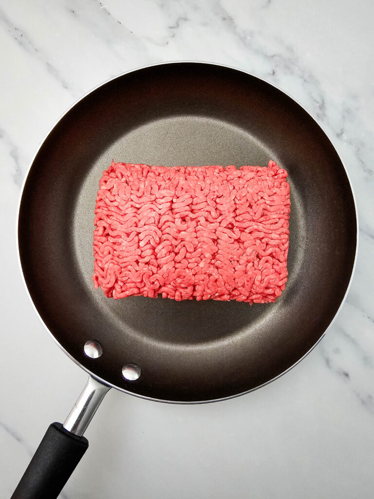 Raw ground beef placed in a skillet before cooking for sheet pan nachos.