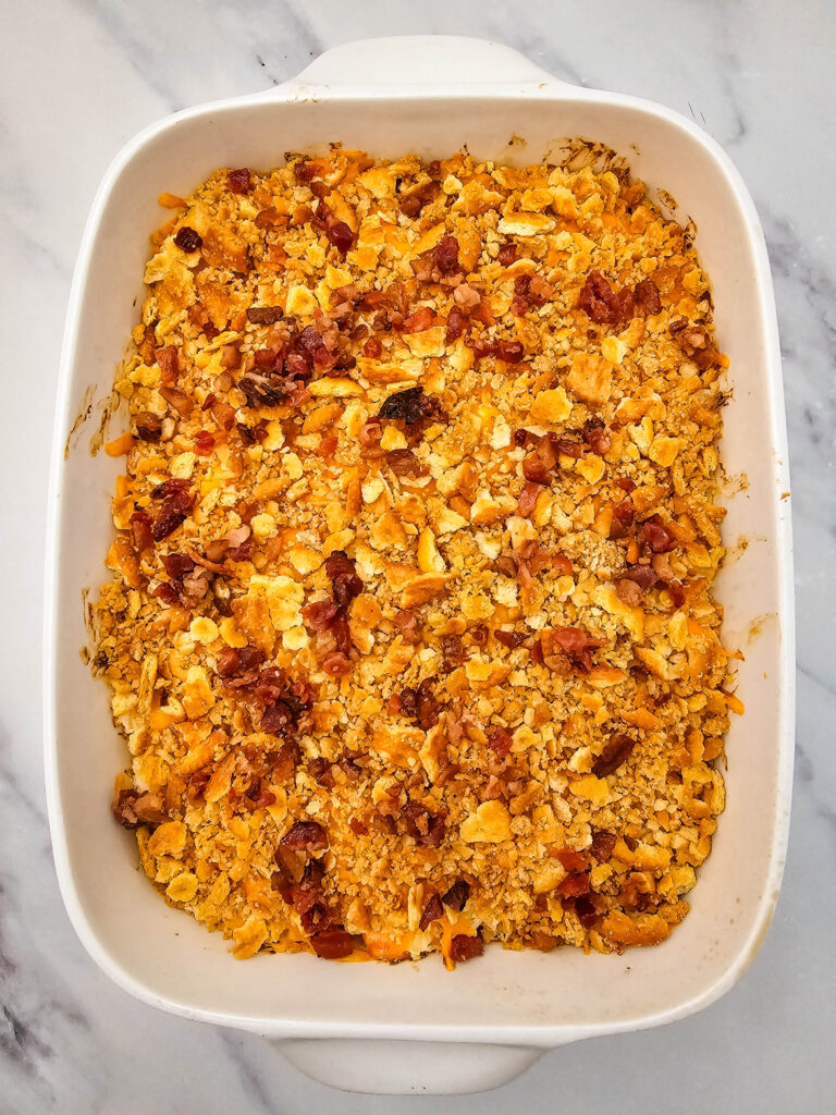Million Dollar Potato Casserole topped with golden crackers and bacon pieces before adding green onions