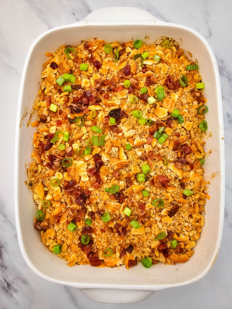 Million Dollar Potato Casserole finished with bacon pieces and sliced green onions in a white baking dish.