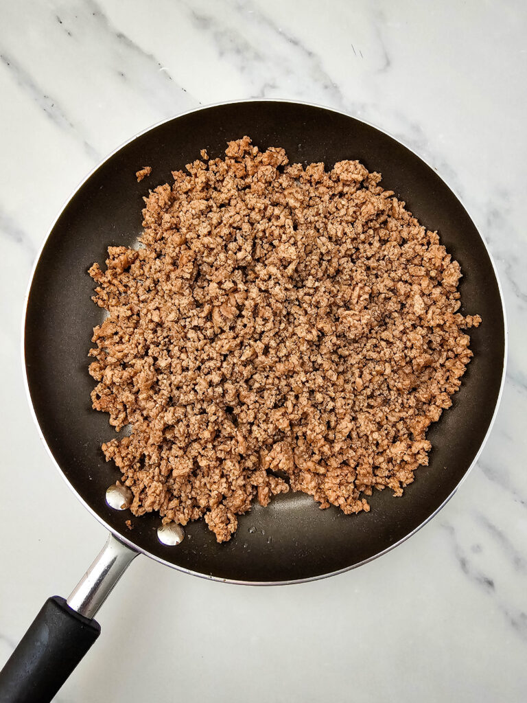 Cooked ground beef crumbles in a skillet for sheet pan nachos.