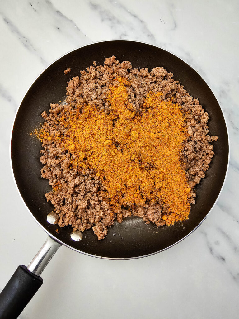 Taco seasoning added to cooked ground beef in a skillet.