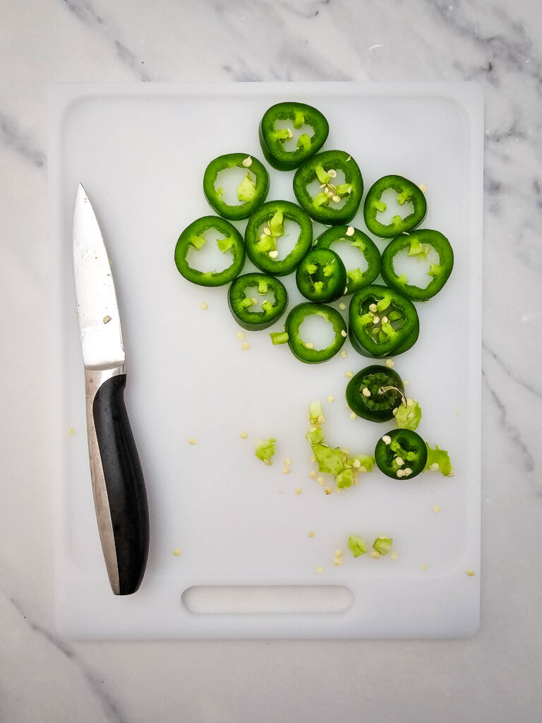 Sliced jalapeños on a white cutting board with a knife.
